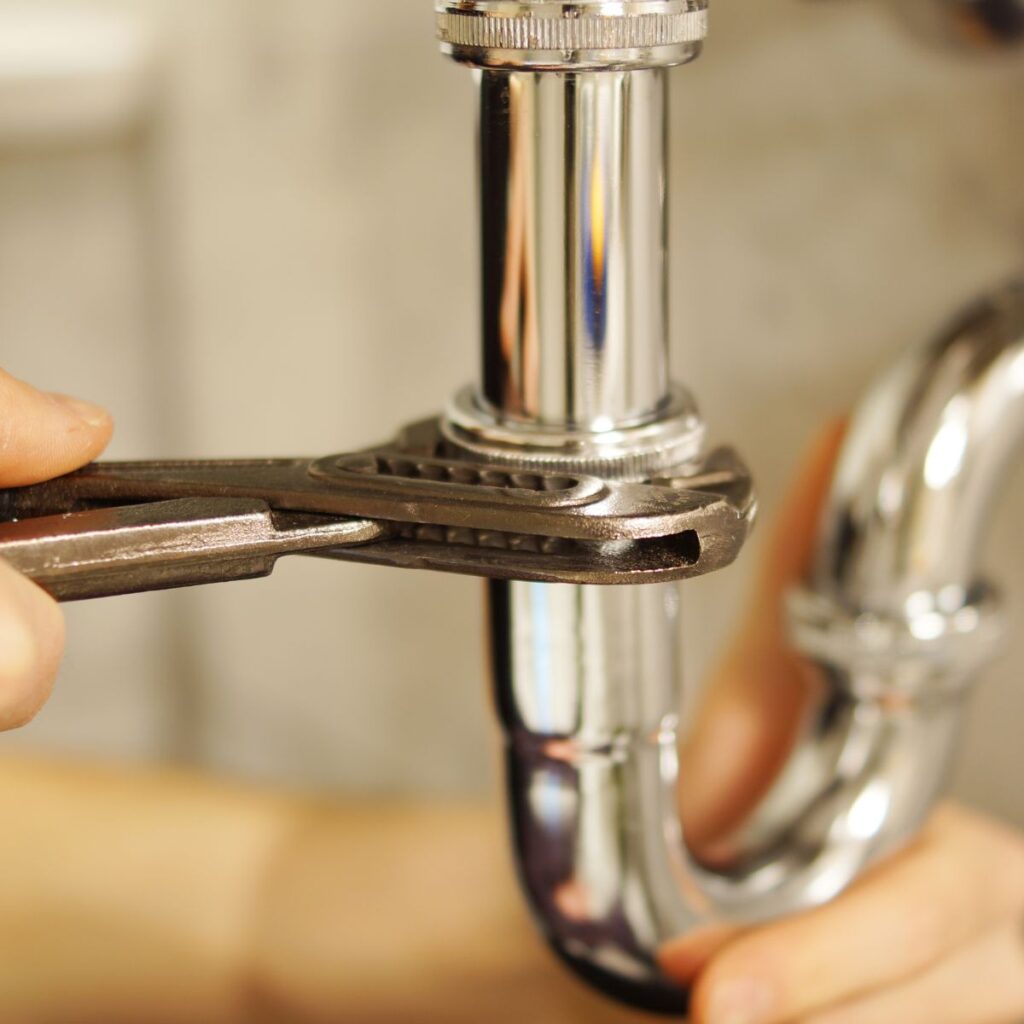 Close-up of a hand using a wrench to tighten a shiny chrome pipe, showcasing quality plumbing supplies for professional and DIY repairs