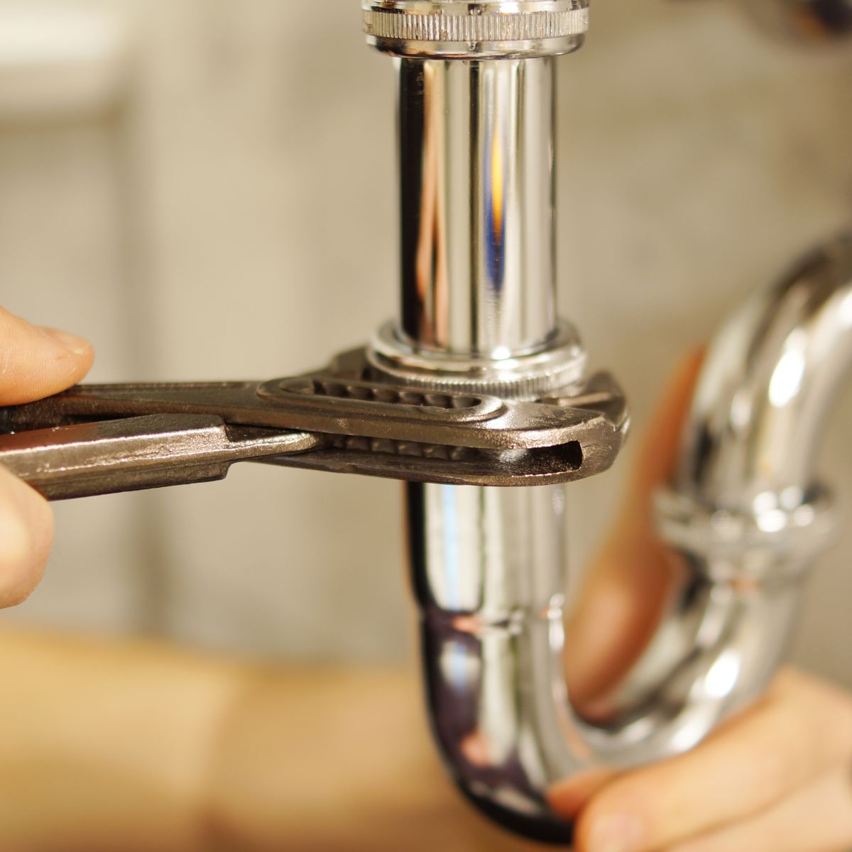 Close-up of a hand using a wrench to tighten a shiny chrome pipe, showcasing quality plumbing supplies for professional and DIY repairs