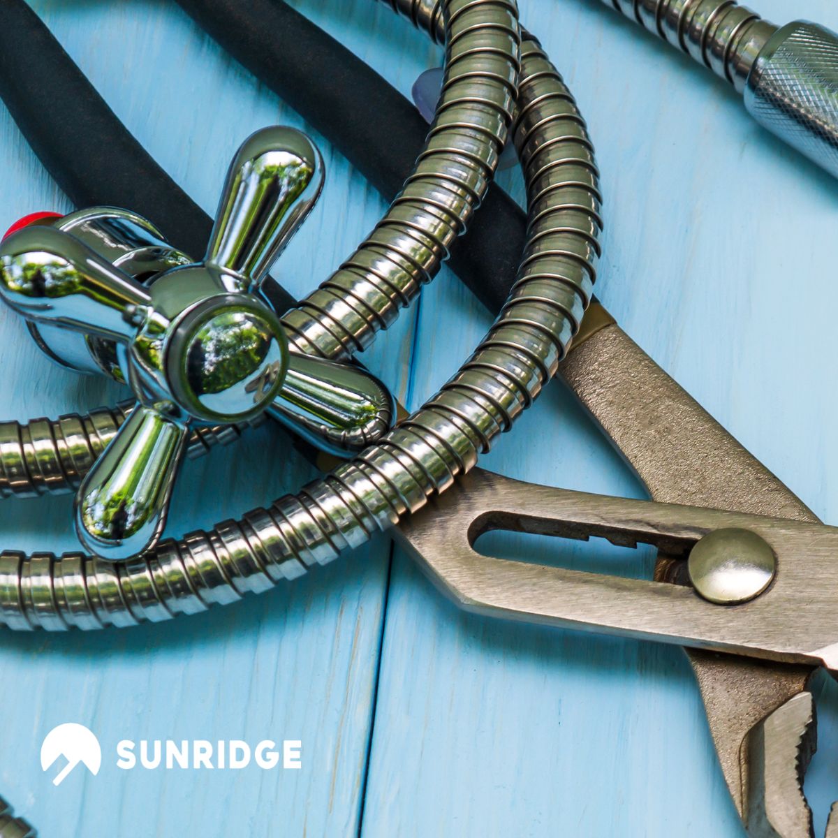 Plumbing tools and chrome faucet hose on wood background featuring sunridge